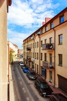 Una calle estrecha flanqueada por edificios de varios pisos, coches aparcados y un cielo despejado.