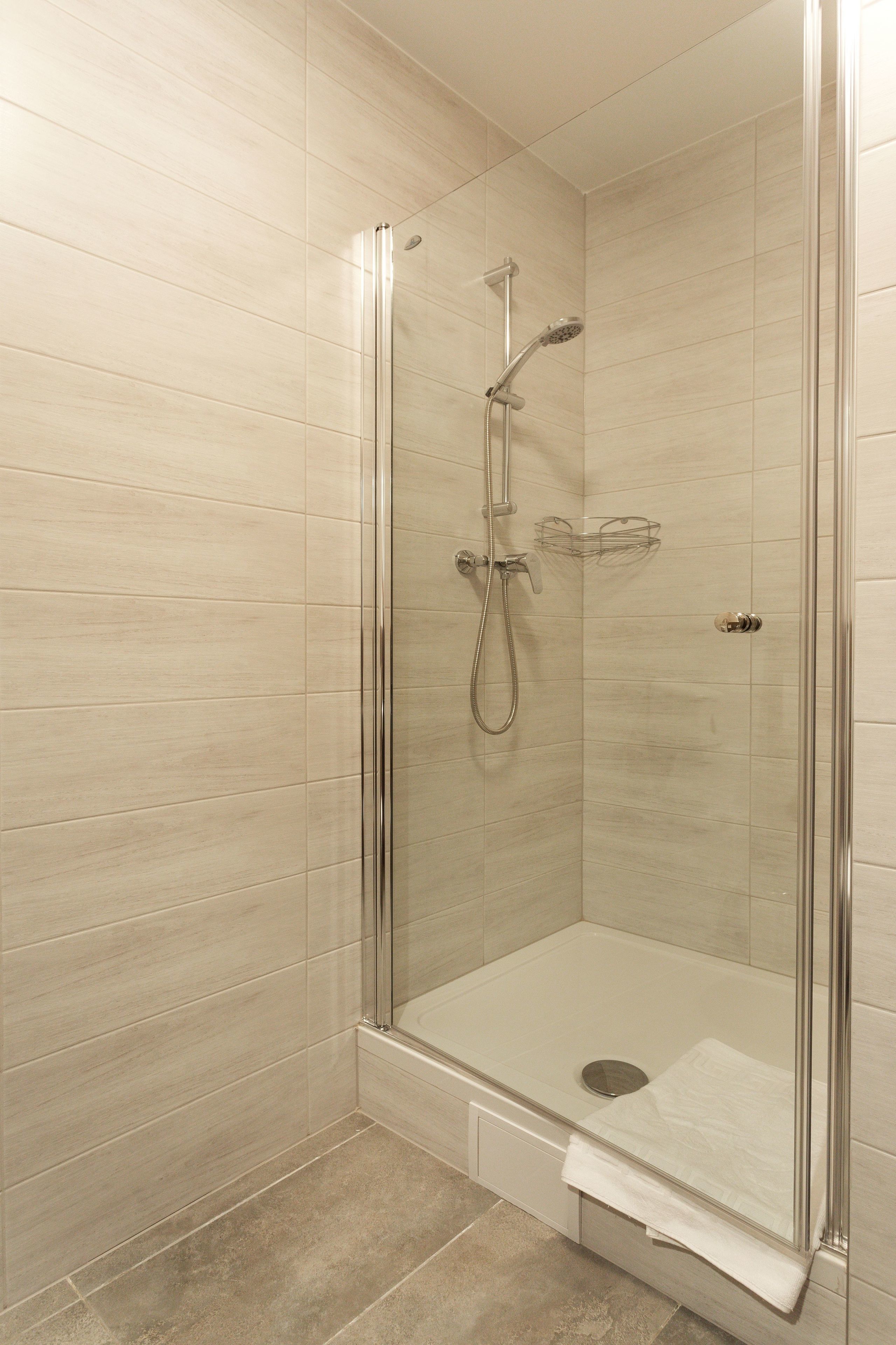 A glass-enclosed shower stall with a handheld showerhead and a wall-mounted faucet.