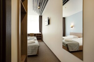 Habitación de hotel con dos camas, televisor, escritorio y espejo.