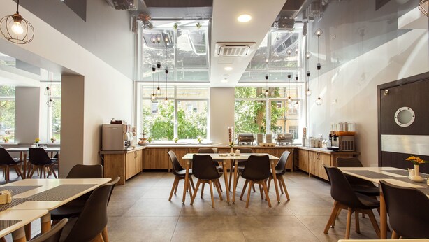 A modern dining area with high ceilings, large windows, and a mix of wooden and upholstered furniture.