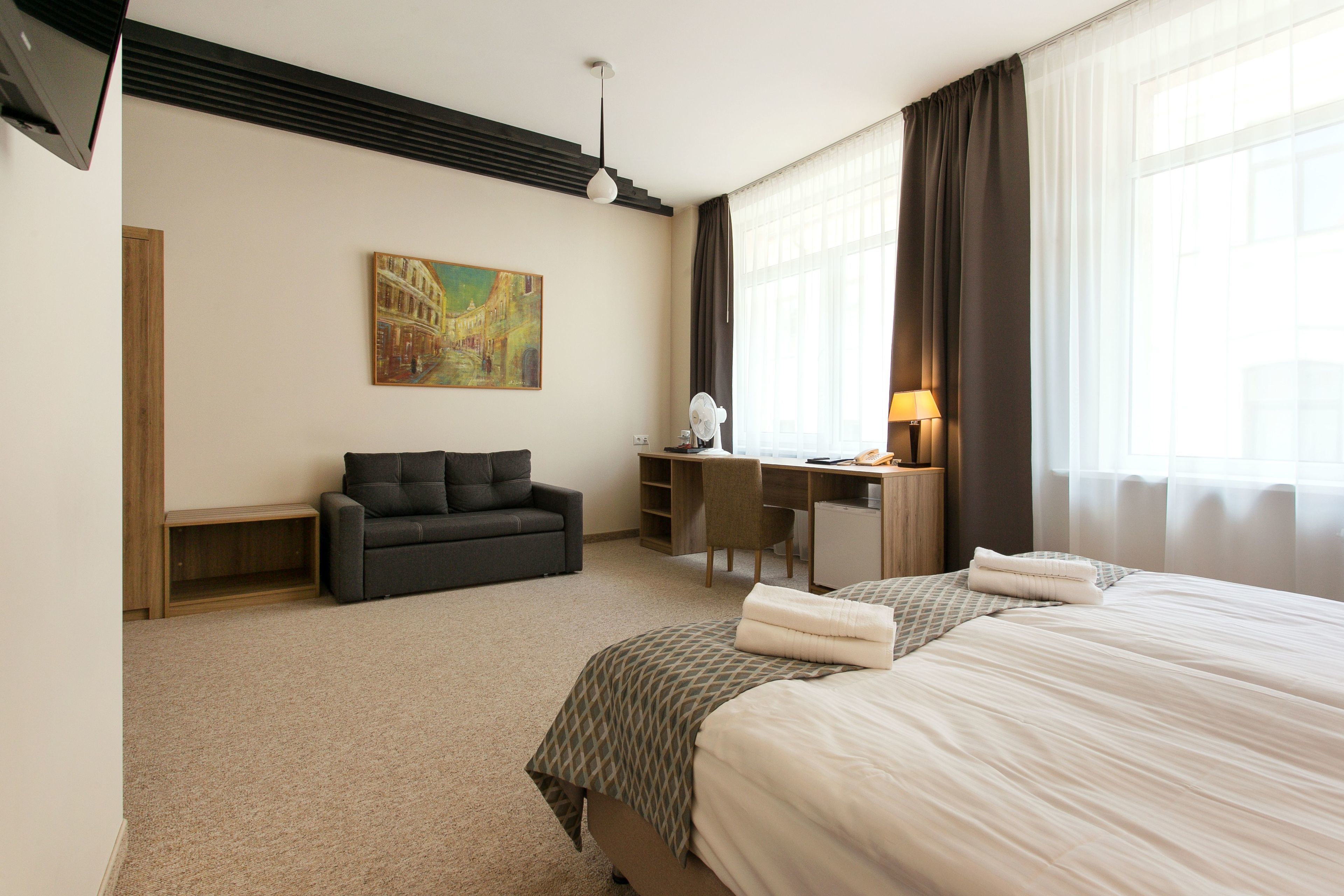 Ett hotellrum med en säng, ett skrivbord, en stol, en soffa, en tavla och en lampa.