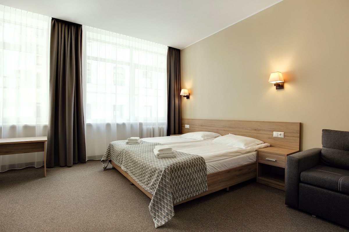 A hotel room with a bed, bedside tables, a bench, and a chair.