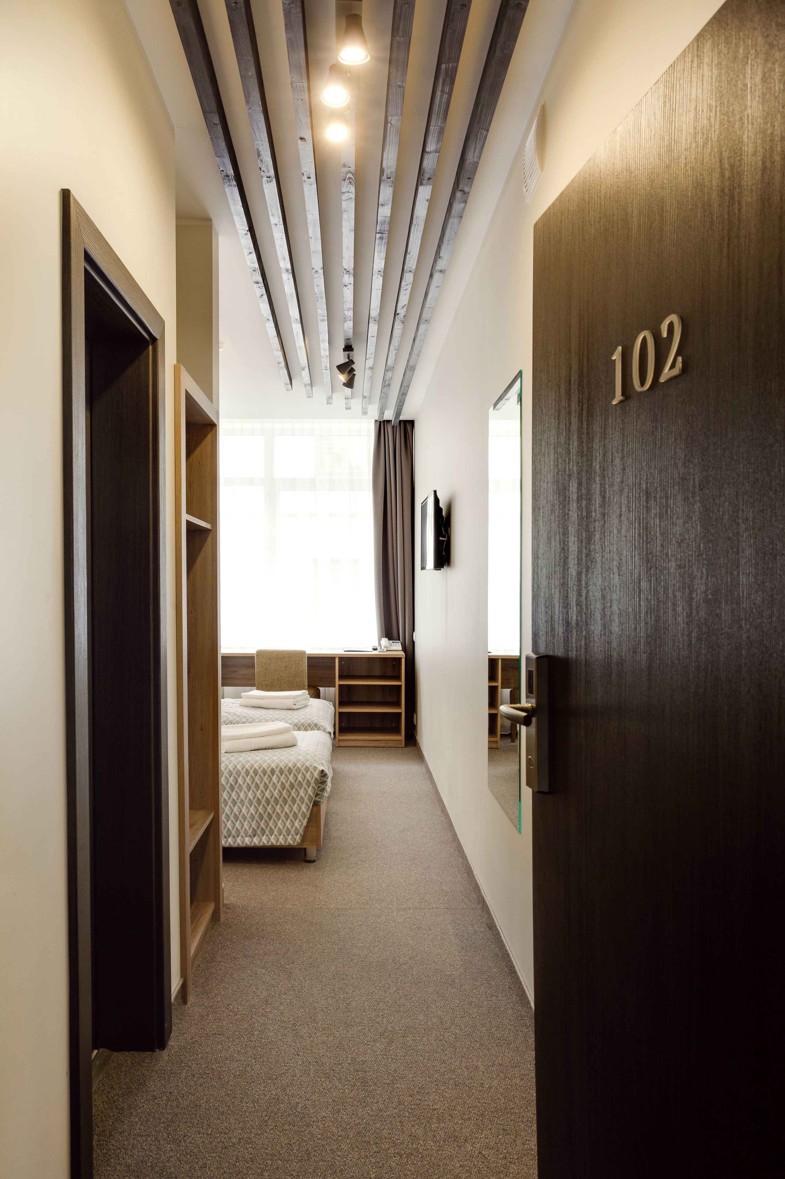 A narrow hallway with a bed, a TV, and a door labeled 102.