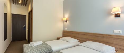 A hotel room with two beds, a wooden headboard, a wall-mounted lamp, and a door.