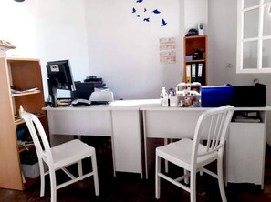 Una oficina pequeña con dos sillas blancas, un escritorio con un ordenador y una estantería.