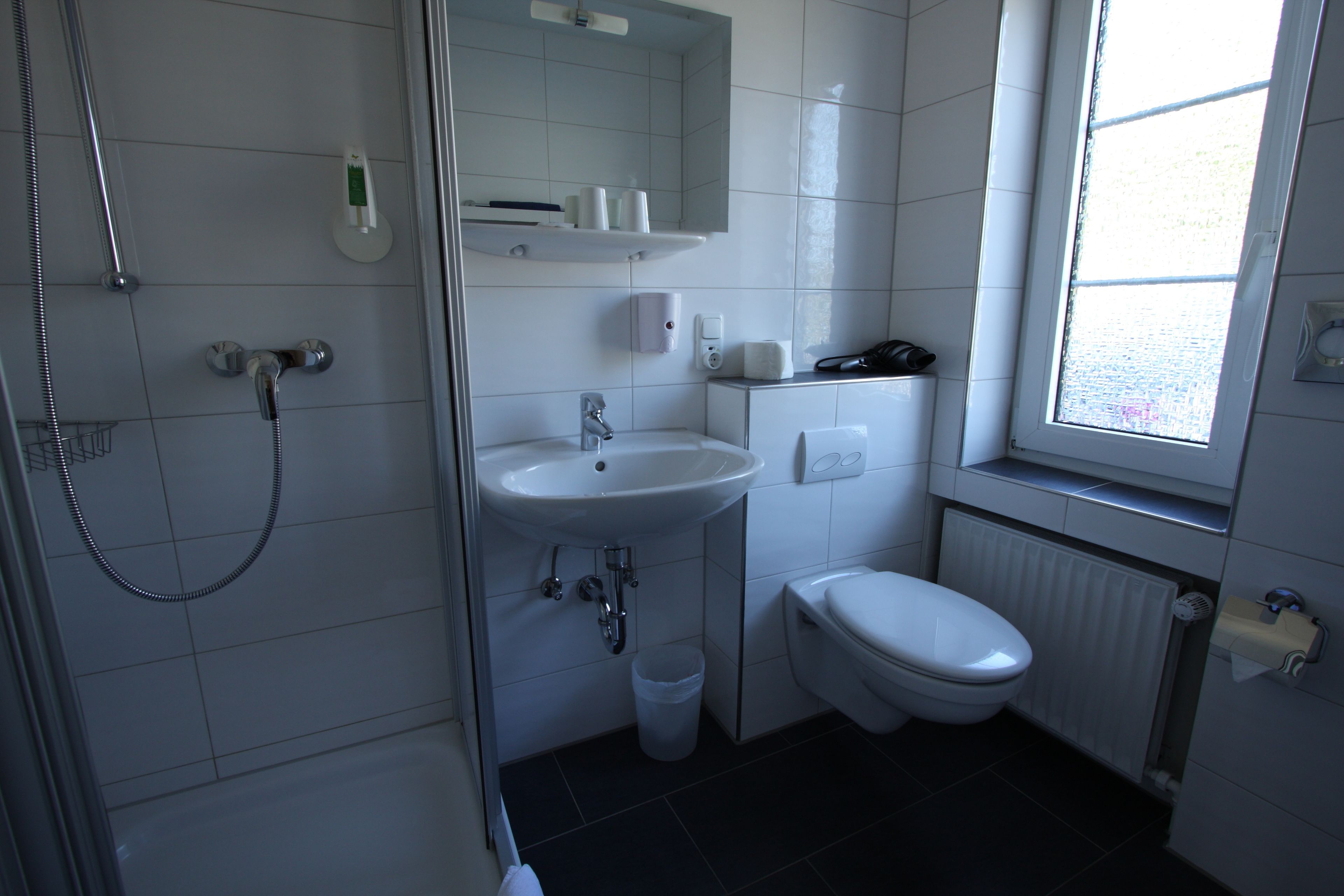 A modern bathroom with a shower, sink, toilet, and a window providing natural light.