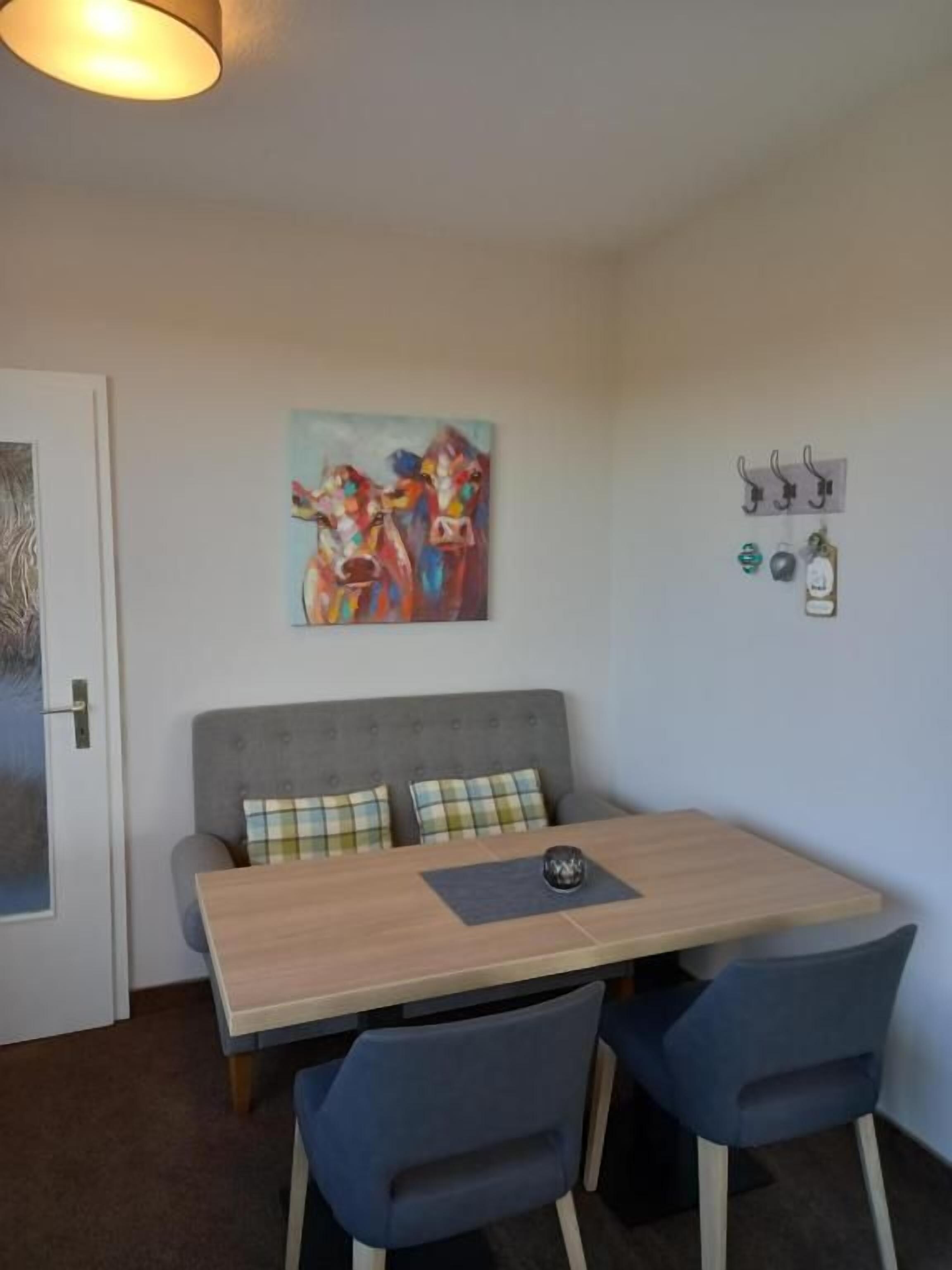 Een kleine kamer met een bank, een tafel en stoelen. Er hangt een schilderij aan de muur en aan haken liggen sleutels.