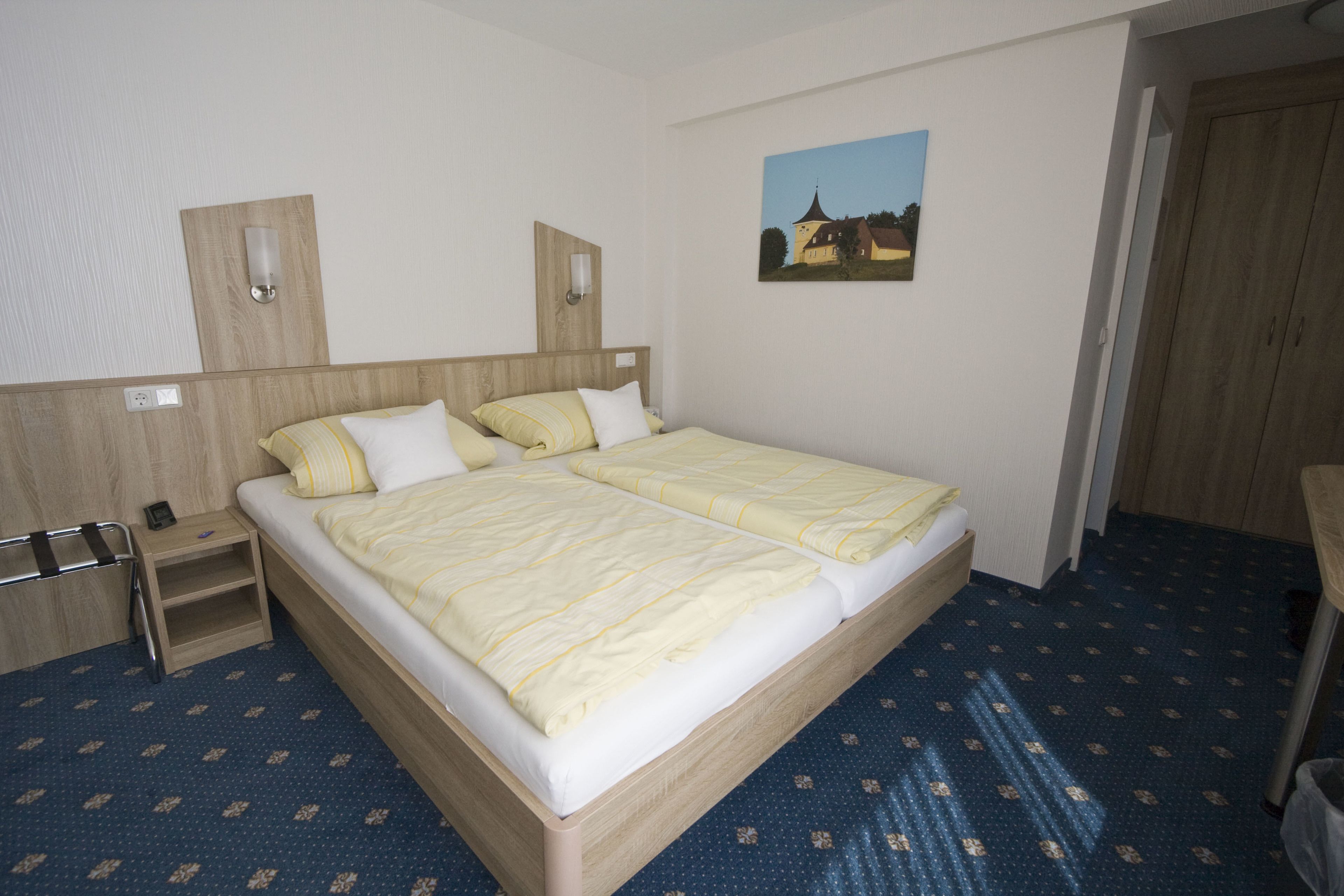 A double bed with a wooden headboard, a bedside table, and a wall-mounted lamp.