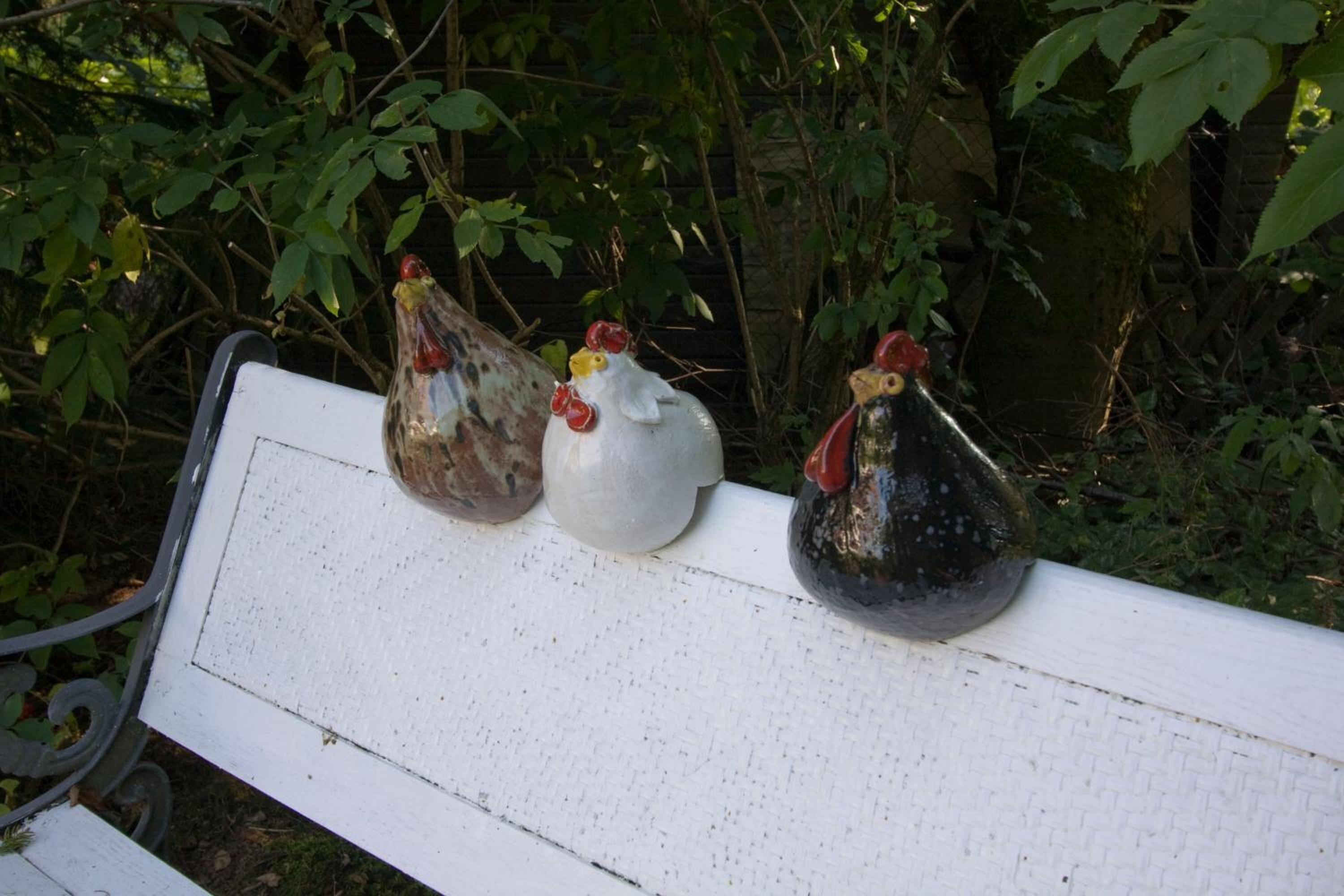 Three ceramic chickens on a white bench.
