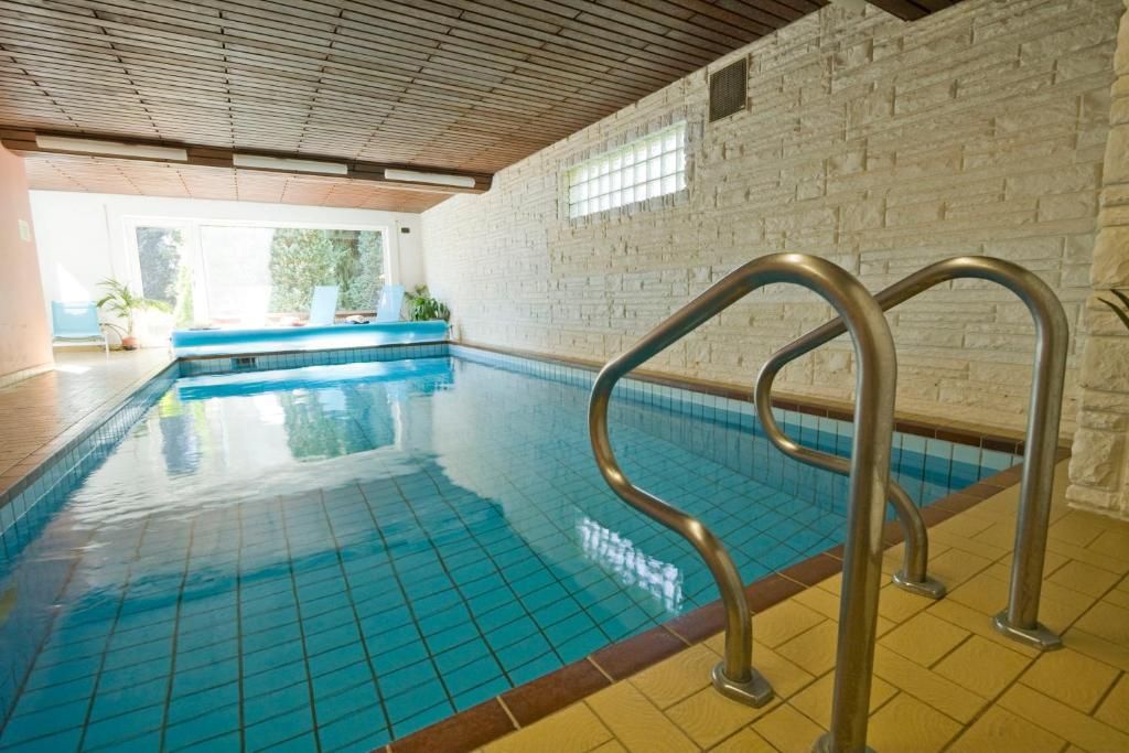 An indoor swimming pool with clear blue water, a wooden ceiling, and a brick wall.