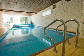 Una piscina interior con agua azul cristalina, techo de madera y pared de ladrillo.