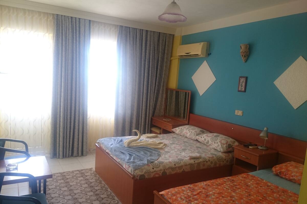 Ett hotellrum med en säng, ett skrivbord, en stol, ett bord och ett fönster med gardiner.