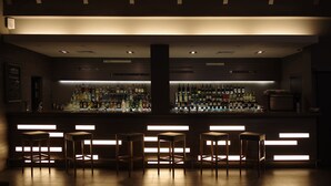 Una zona de bar con una barra larga, varias botellas de licor y varios taburetes.