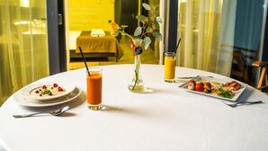 Una mesa de comedor con un plato de comida, un vaso de jugo de naranja y un florero con una flor.