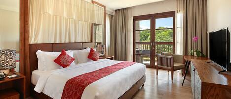A hotel room with a large bed, a desk with a TV, a balcony with a view, and a wooden floor.