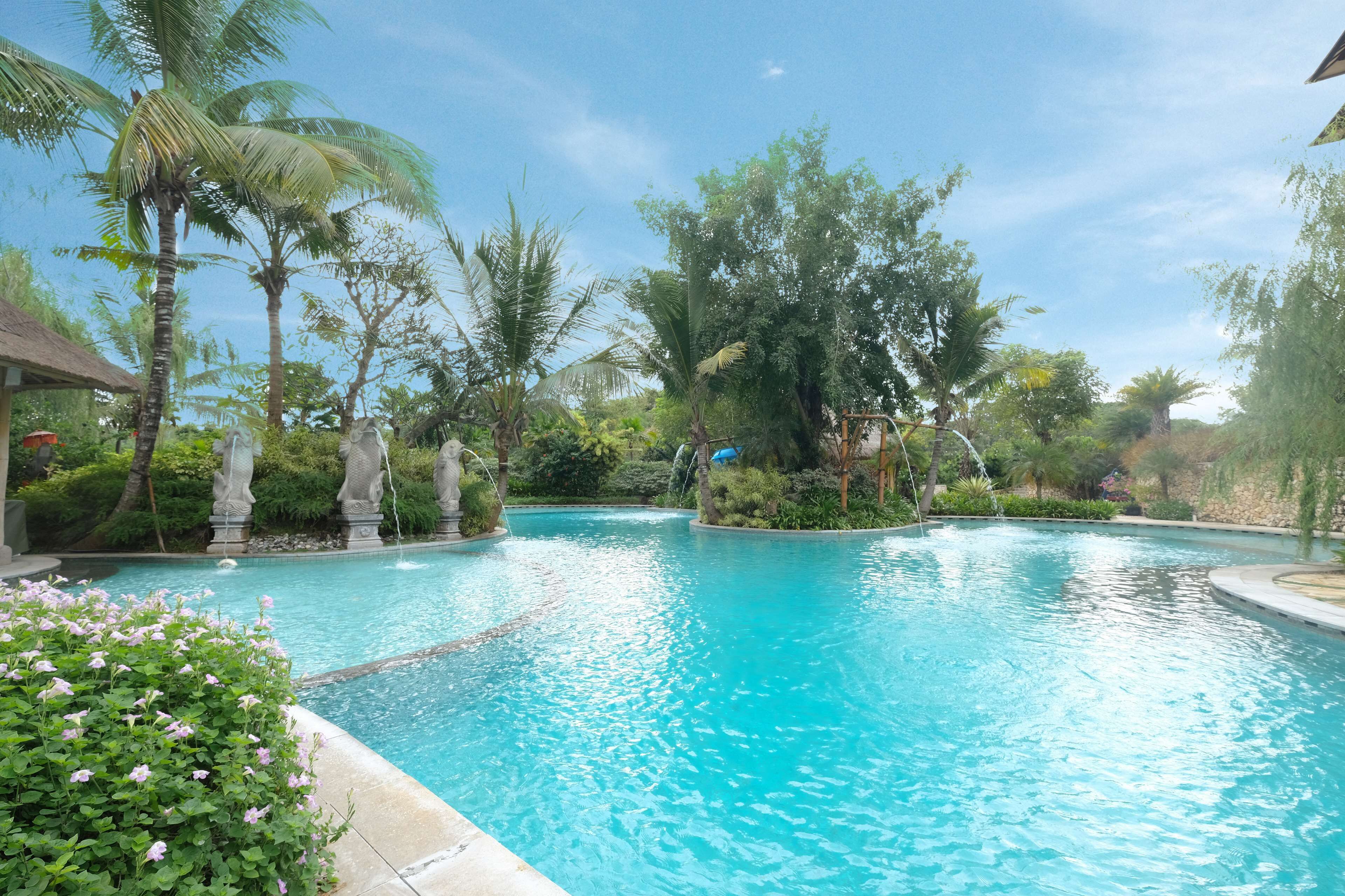 A swimming pool surrounded by tropical plants and a stone structure.