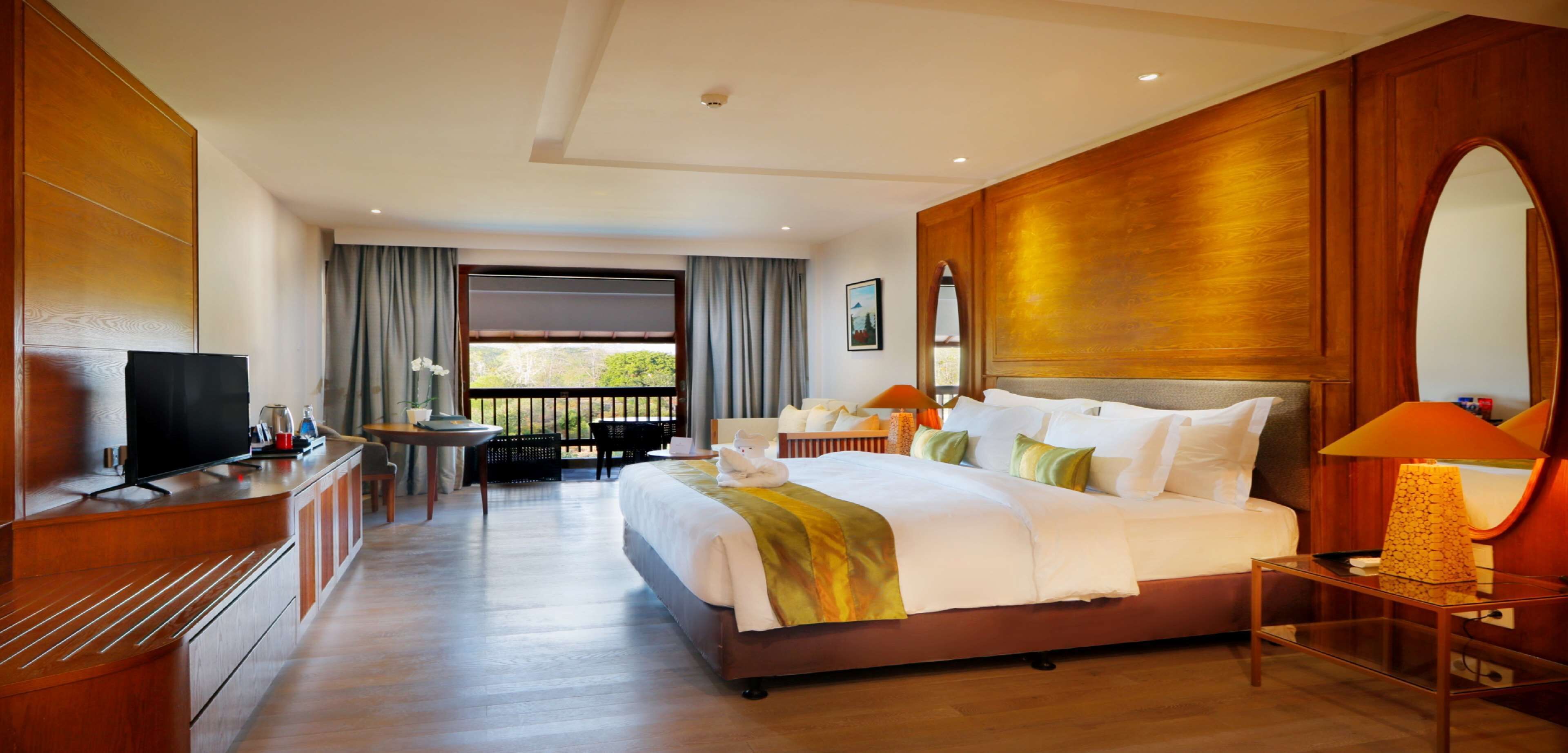A hotel room with a large bed, a desk with a chair, a television, and a balcony with curtains.
