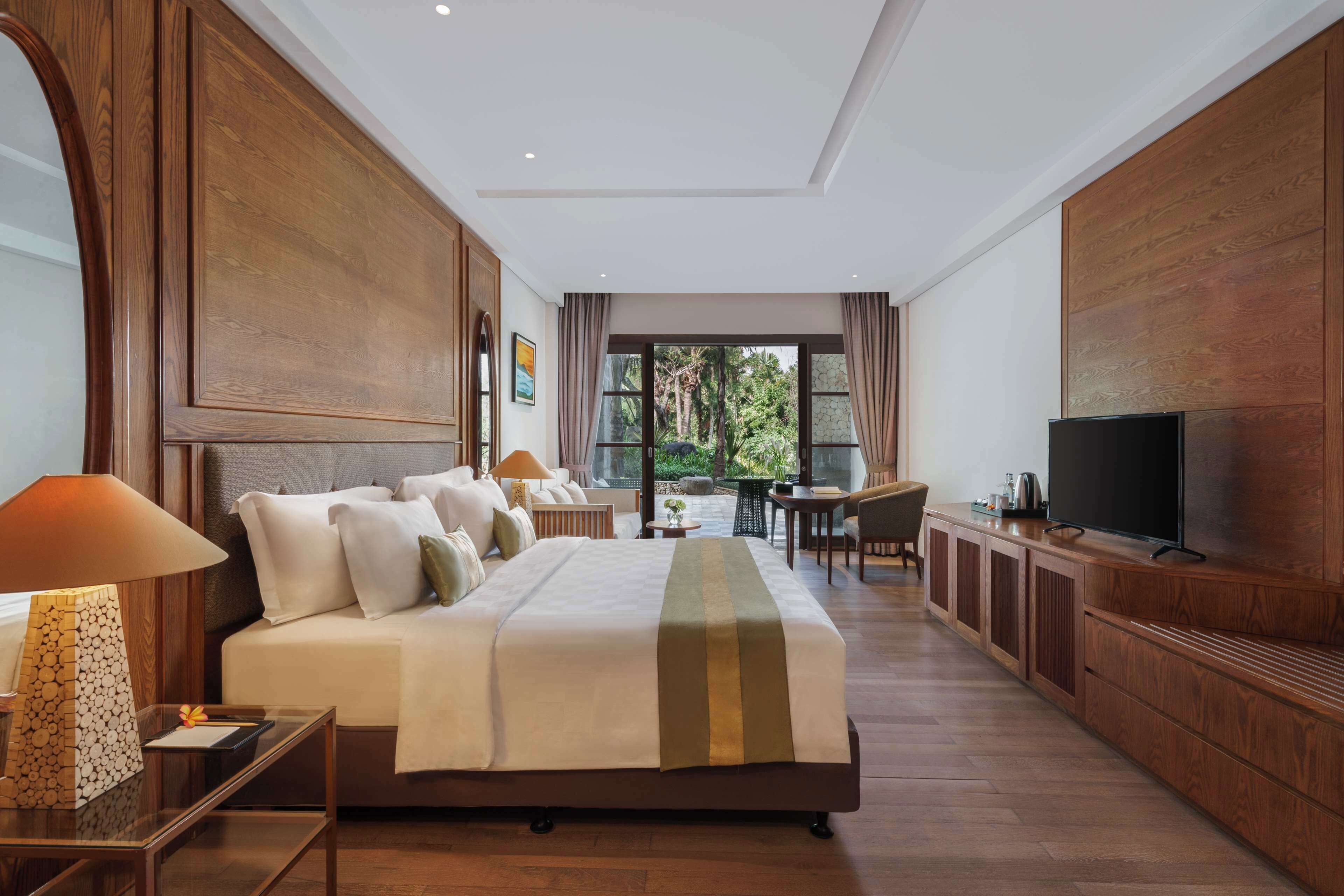 A spacious hotel room with a large bed, a television, a desk, and a view of the outdoors.