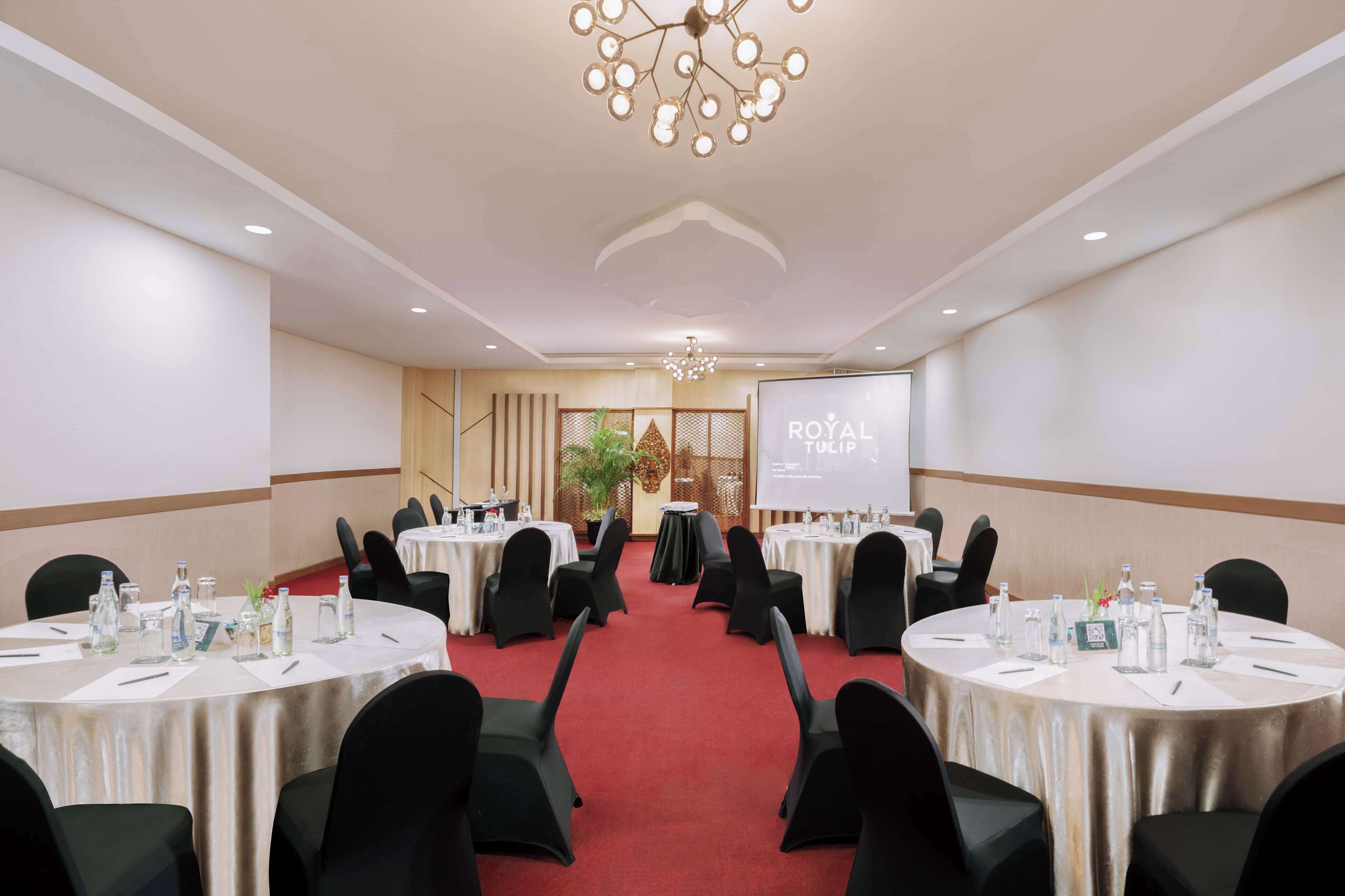 Un salón de conferencias con mesas redondas, sillas negras y una pantalla de proyector que muestra 'ROYAL TRIP'.