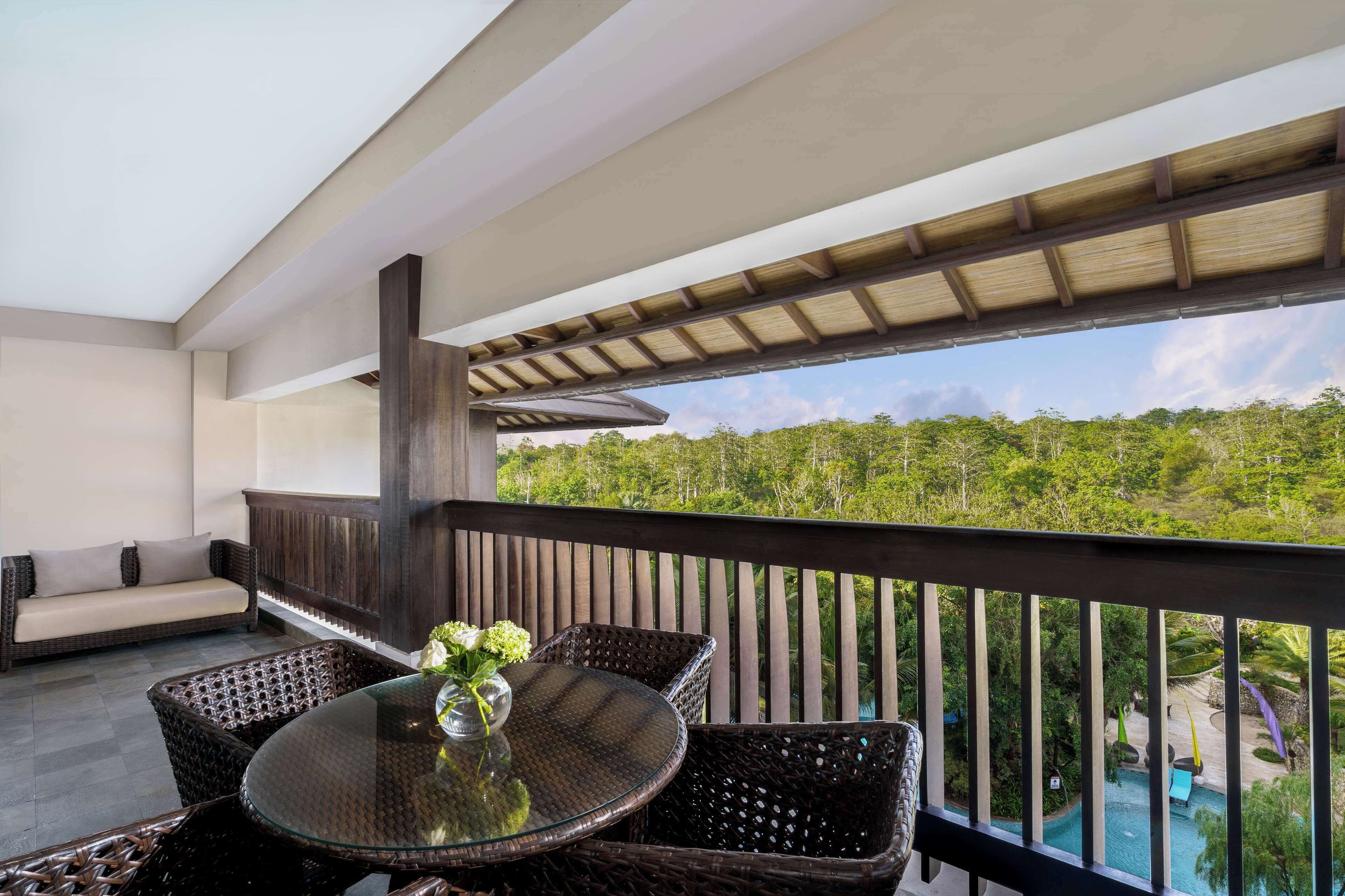 Ein Balkon mit Korbmöbeln, einem Glastisch und Blick auf Pool und Grünflächen.