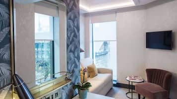 A modern hotel room with a large mirror, a sofa, a small table, a potted plant, and a television on the wall.