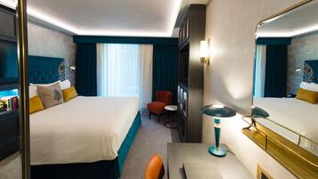 Habitación de hotel con una cama grande, un escritorio con lámpara, una silla, una mesita y una estantería.