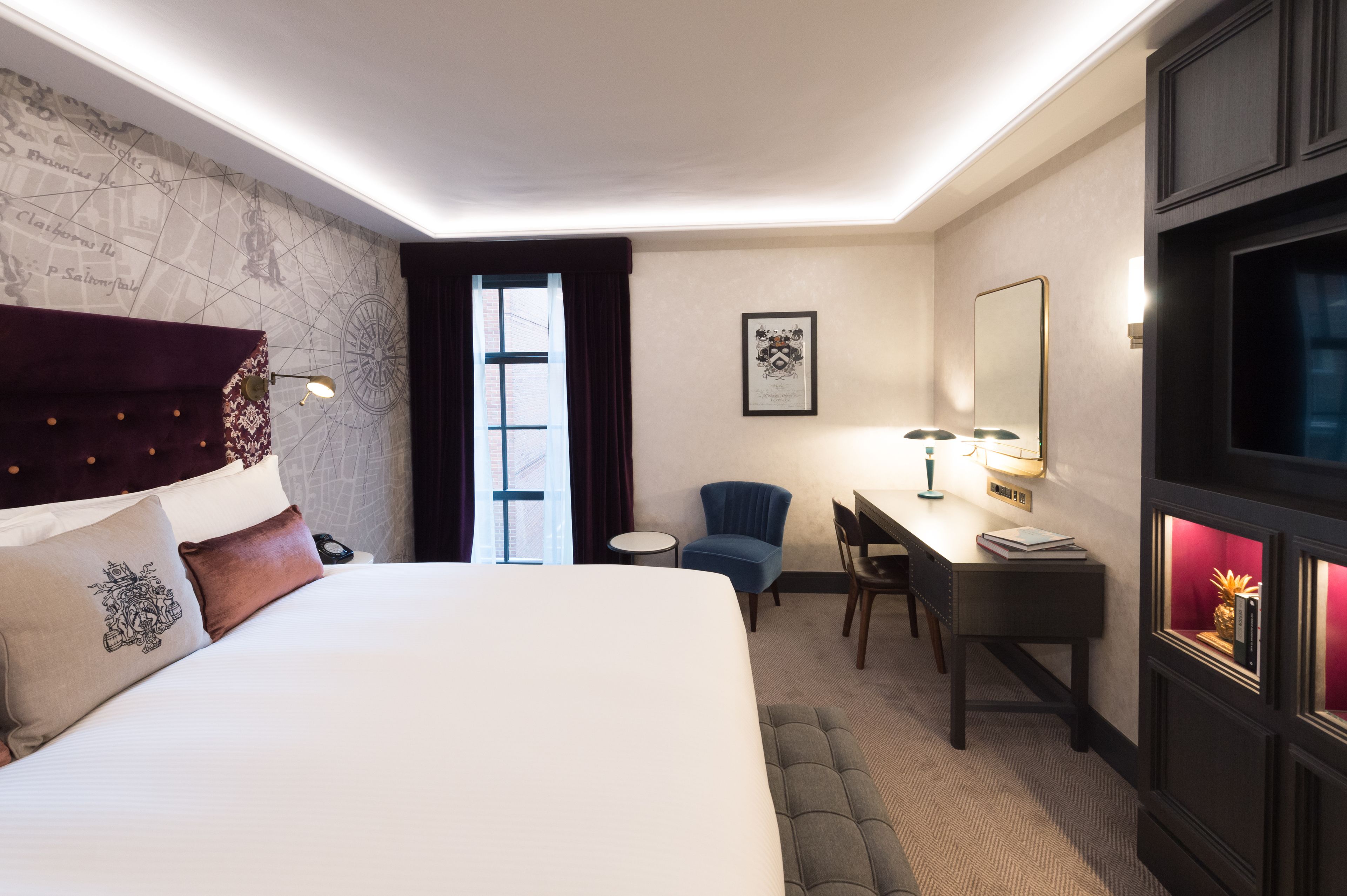 Une chambre d’hôtel avec un grand lit, un bureau, une chaise, une carte accrochée au mur et une fenêtre avec des rideaux.