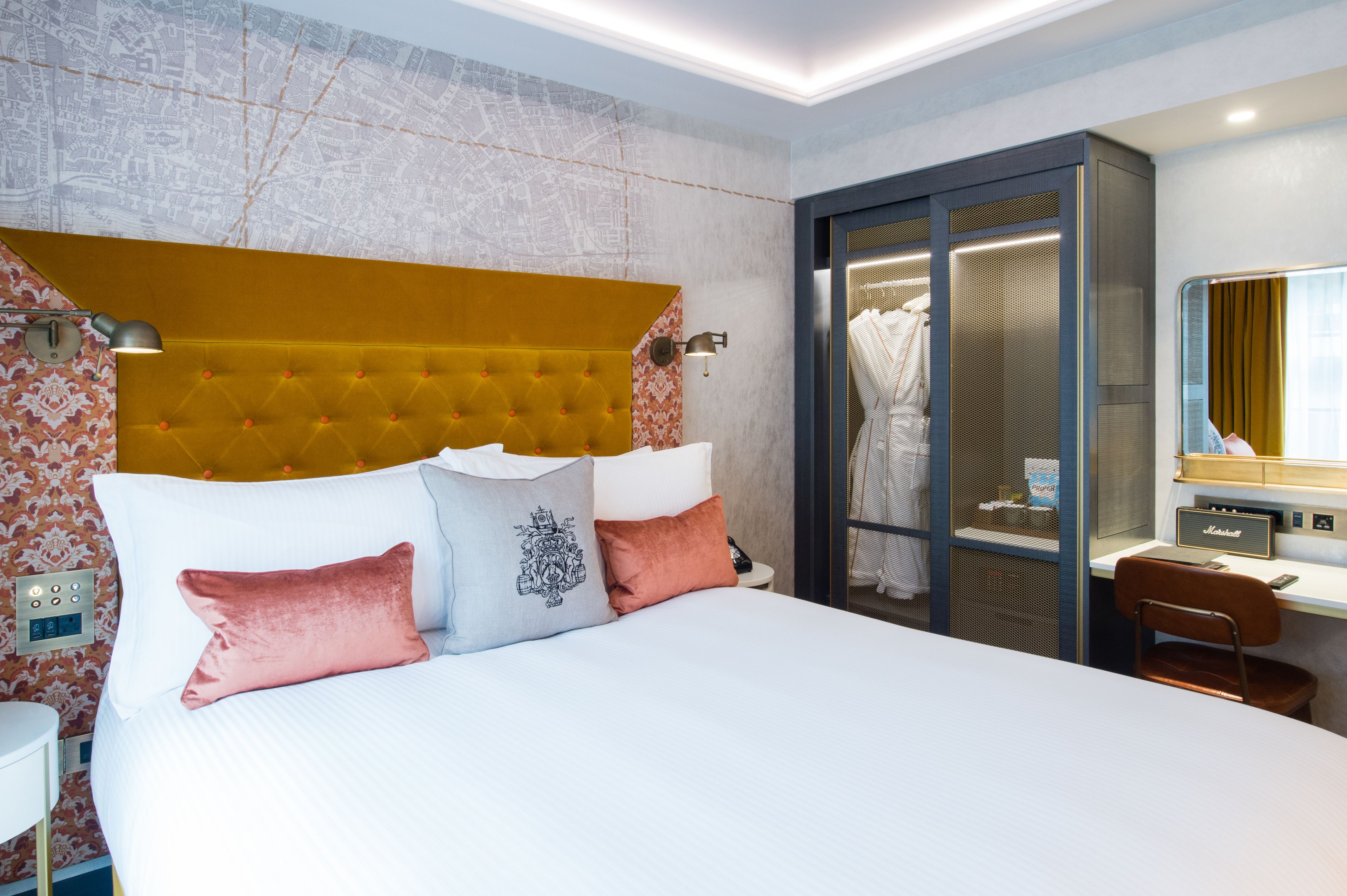 Ein Hotelzimmer mit einem großen Bett, einem Schreibtisch mit Computer, einem Kleiderschrank und einem durch eine Glastür einsehbaren Badezimmer.