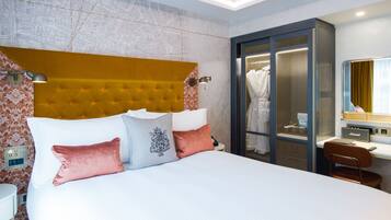 Ein Hotelzimmer mit einem großen Bett, einem Schreibtisch mit Computer, einem Kleiderschrank und einem durch eine Glastür einsehbaren Badezimmer.