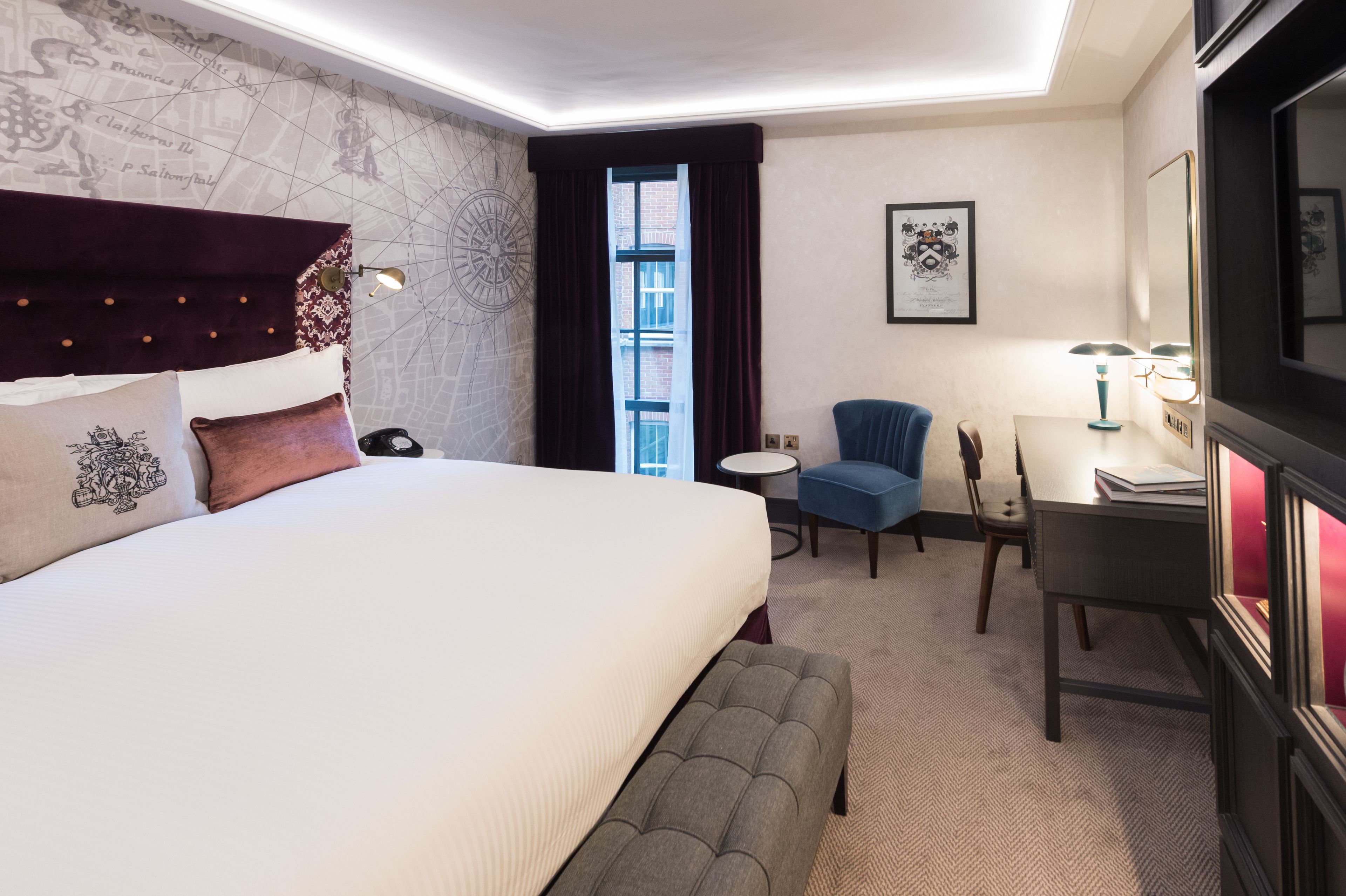 A hotel room with a large bed, a desk, a chair, a small round table, and a window with curtains.