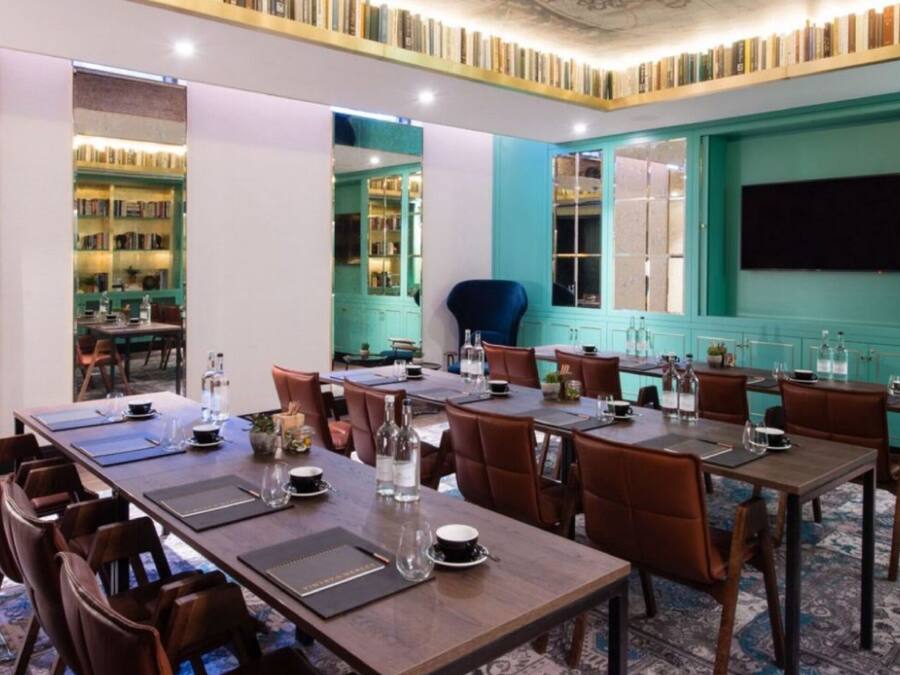 A dining area with multiple tables and chairs, a television mounted on the wall, and bookshelves in the background.