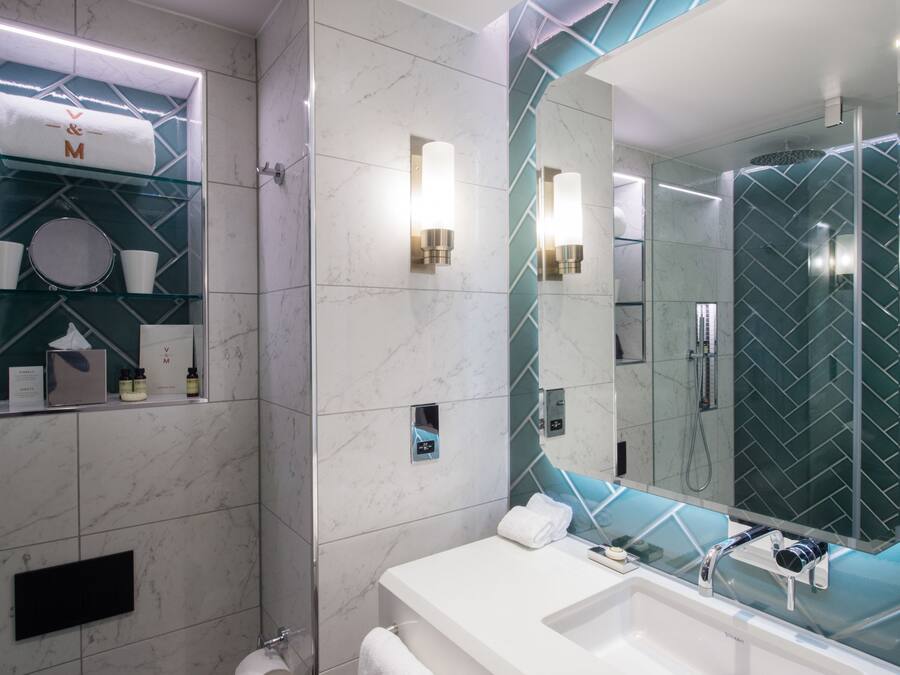Une salle de bain moderne avec une étagère en verre où sont rangés les articles de toilette, un grand miroir et un espace douche.