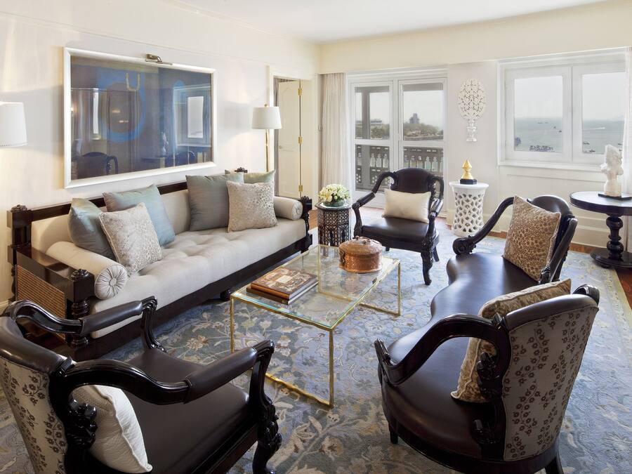 A living room with a sofa, armchairs, a glass coffee table, and a view of the city through large windows.