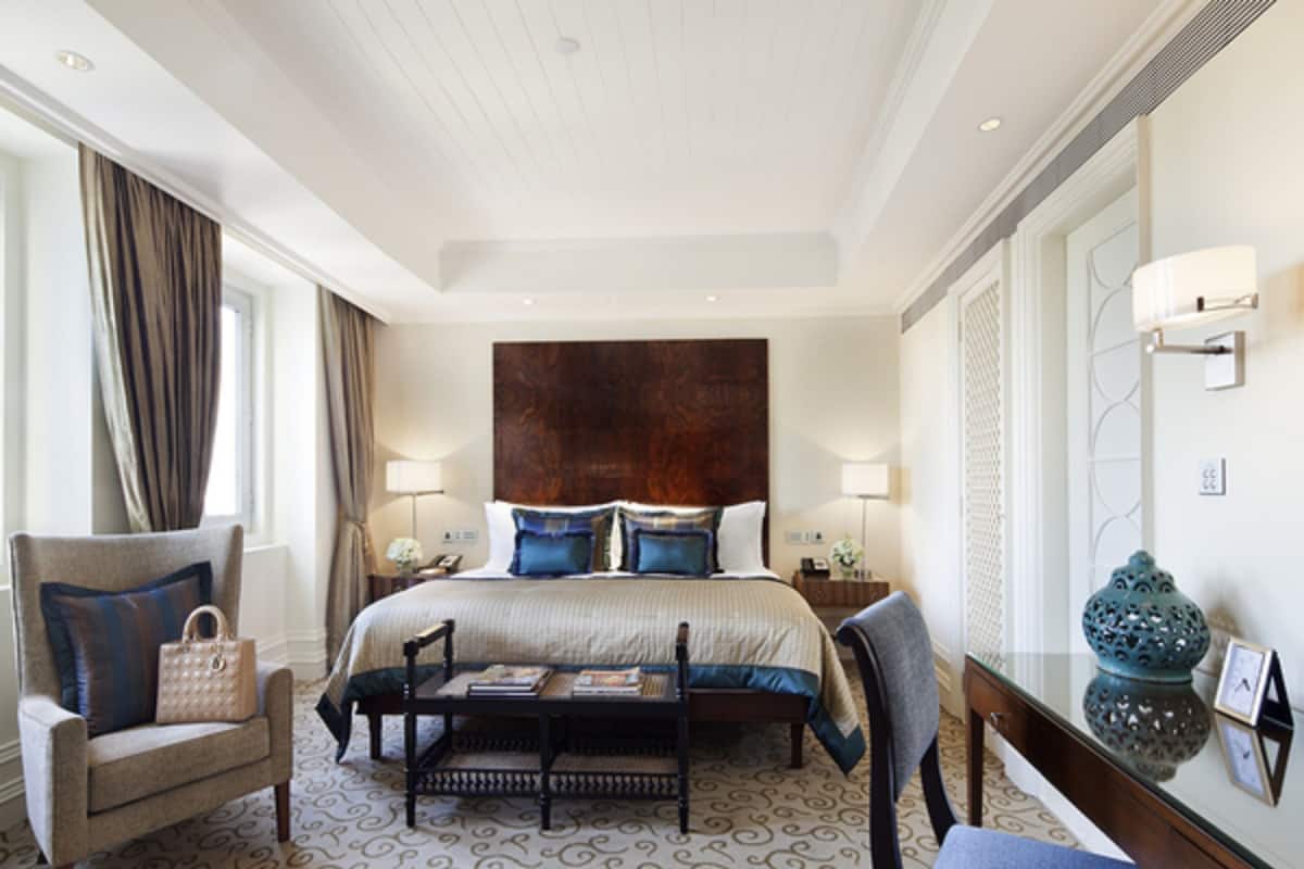 A hotel room with a large bed, two bedside tables, a chair, a small table, and a decorative vase.