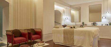 A modern bedroom with a large bed, two red chairs, a mirror, and a wooden floor.