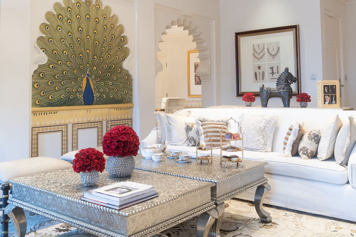 A luxurious living room with a white sofa, a decorative peacock mirror, and a chandelier.