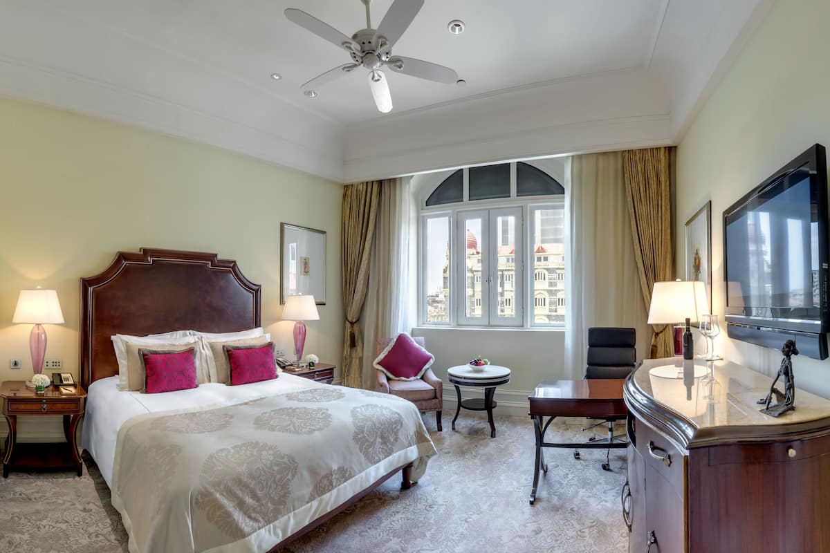 A hotel room with a large bed, a desk, a chair, a TV, and a window with curtains.