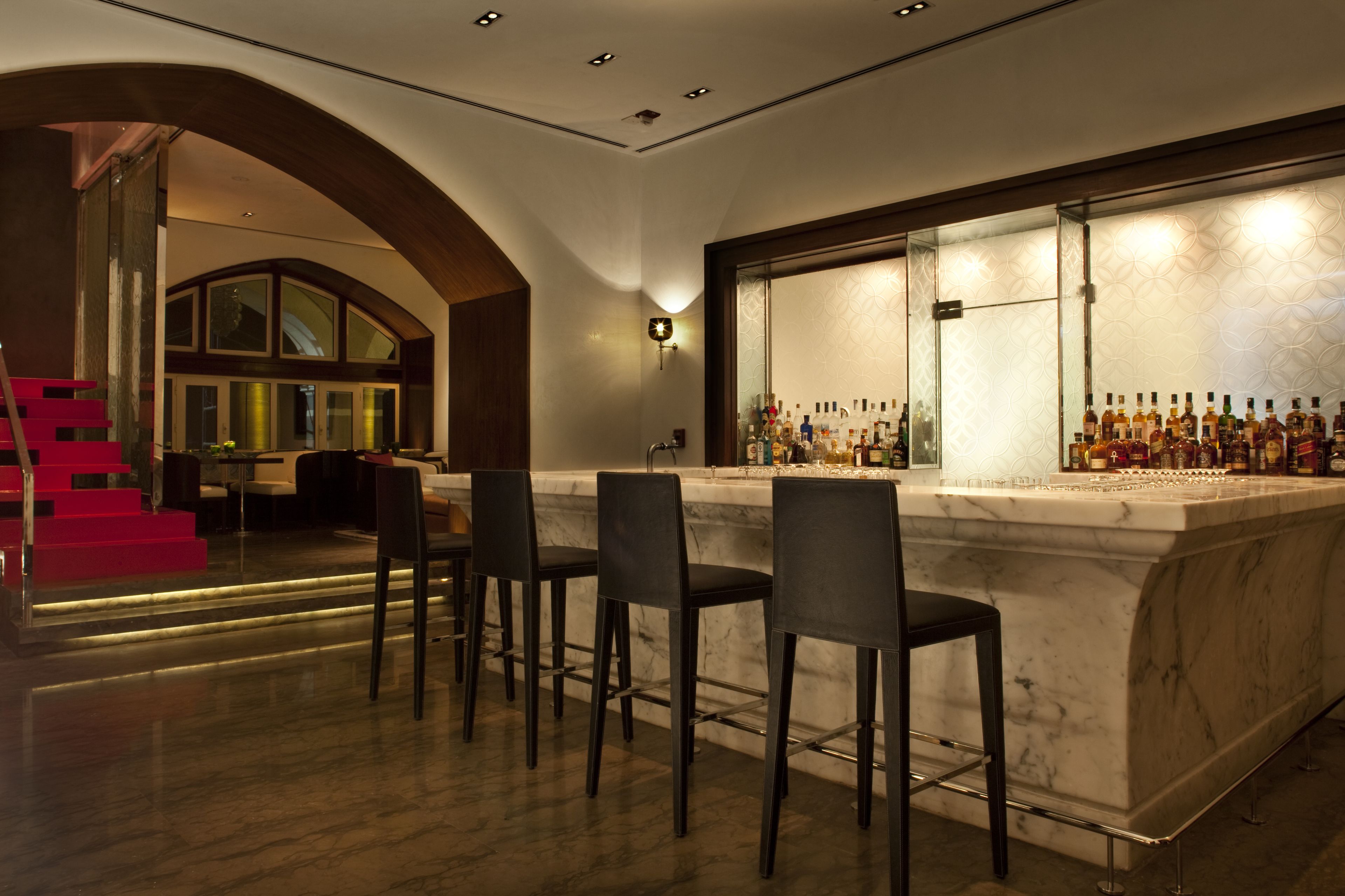 Una zona de bar con encimera de mármol, varios taburetes y una vitrina de vidrio llena de botellas.