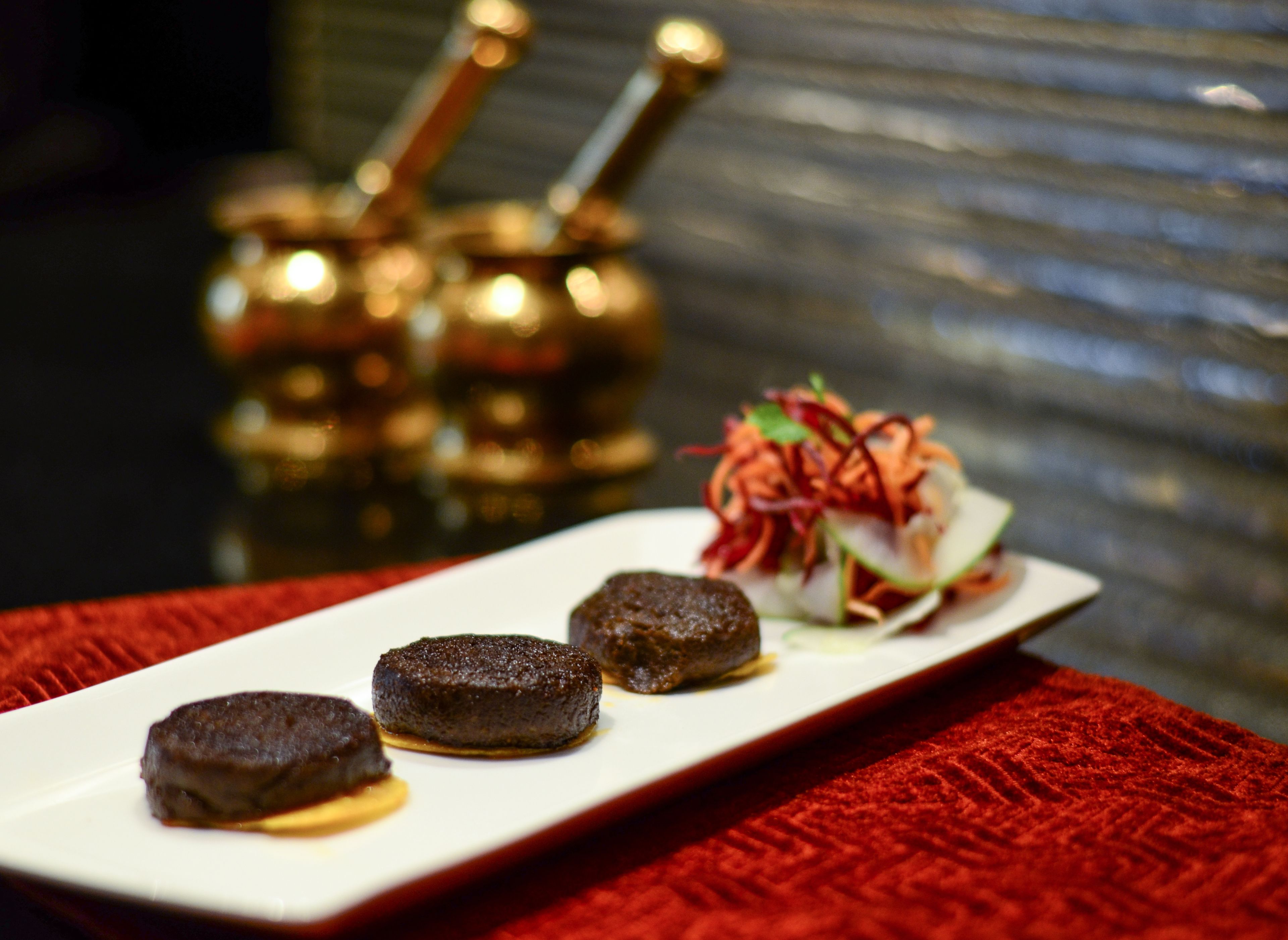 A plate with three round, dark brown items, possibly food, on a white rectangular plate.