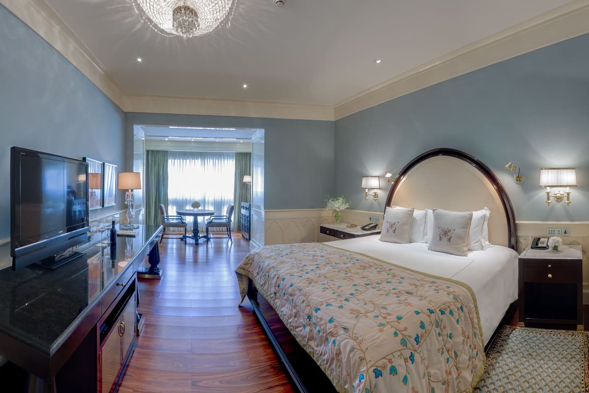 A hotel room with a large bed, a TV, a desk with a chair, and a view of the outdoors.