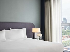 Una habitación de hotel con una cama grande, una mesita de noche con una lámpara y una ventana con cortinas.