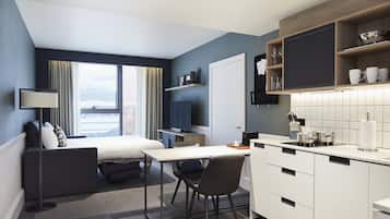 Un moderno cuarto de hotel con cama, escritorio, silla, televisor, kitchenette y vistas a la ciudad.