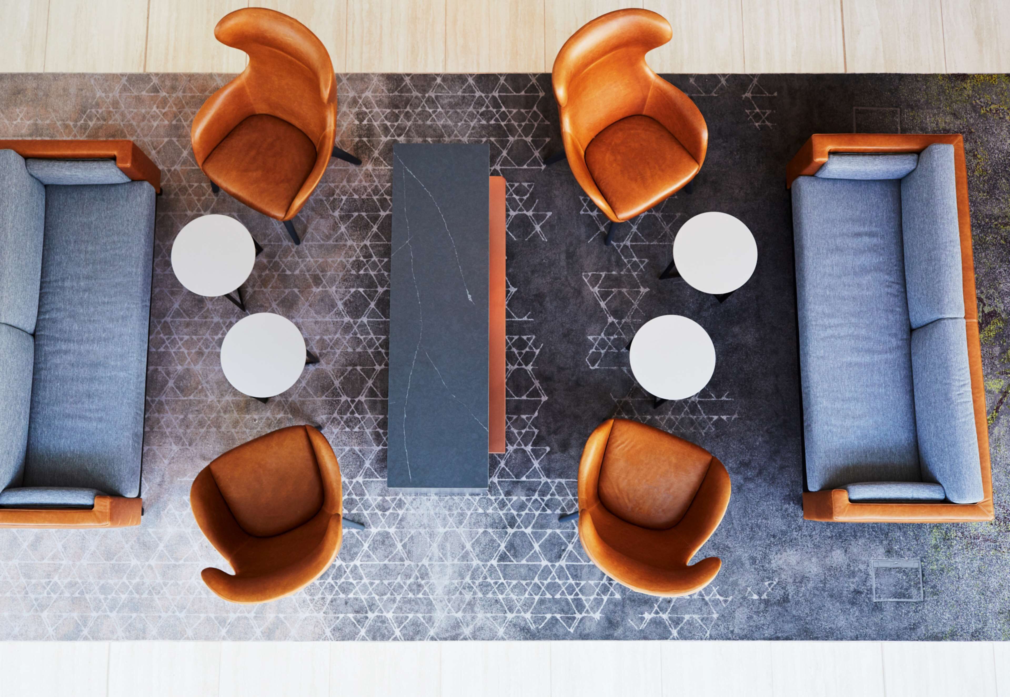 A modern lounge area with sofas and chairs arranged around a central table, with a patterned rug and a geometric floor design.