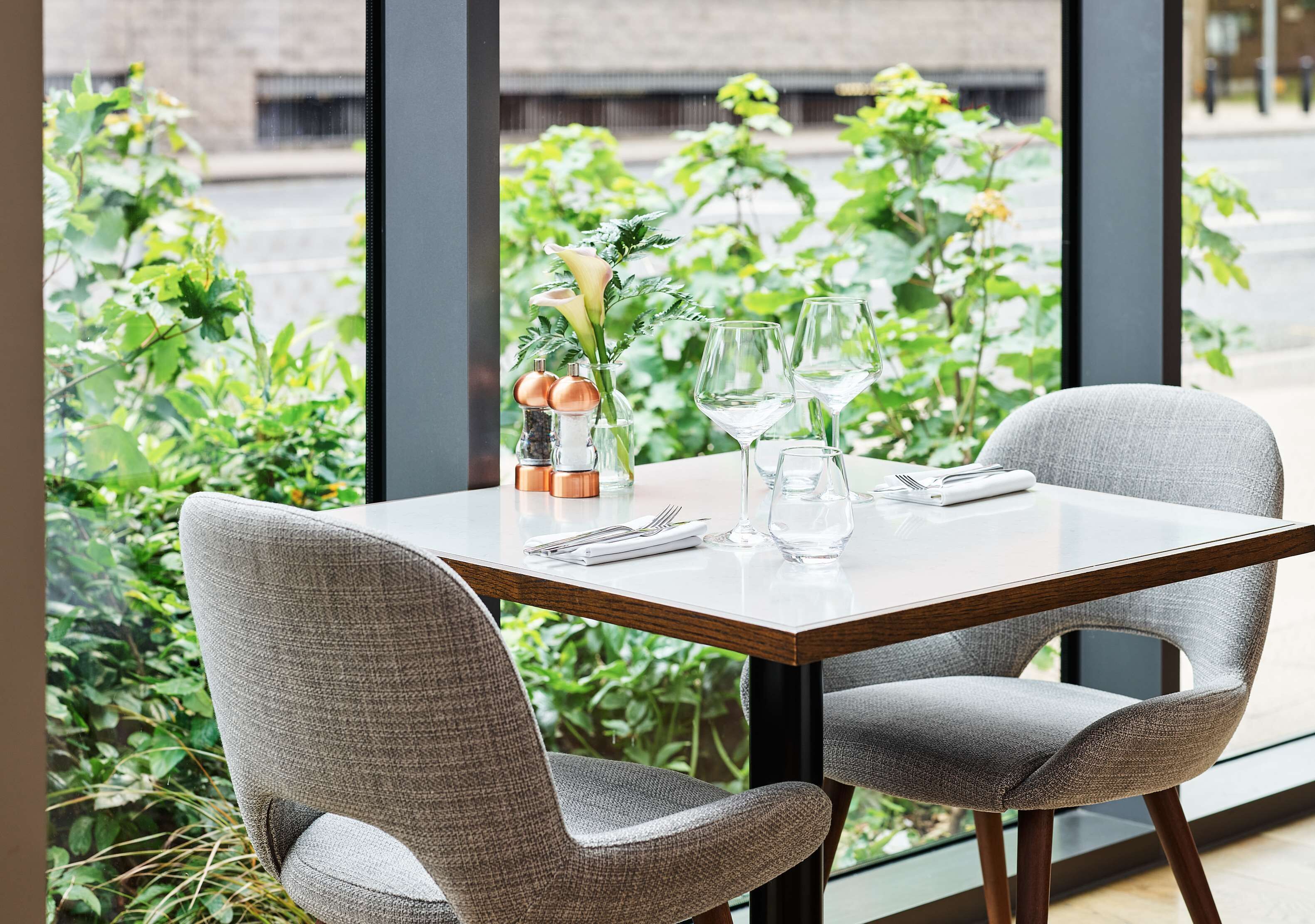 A dining table set with two chairs, a vase with flowers, and wine glasses.