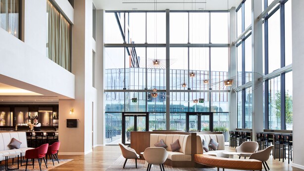 A spacious lobby with a high ceiling, large windows, and a seating area with sofas and chairs. - Hyatt House Manchester - Aparthotel (Manchester)