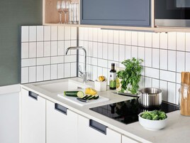 Una cocina moderna con encimera blanca, pileta de acero inoxidable y cocina por inducción negra.