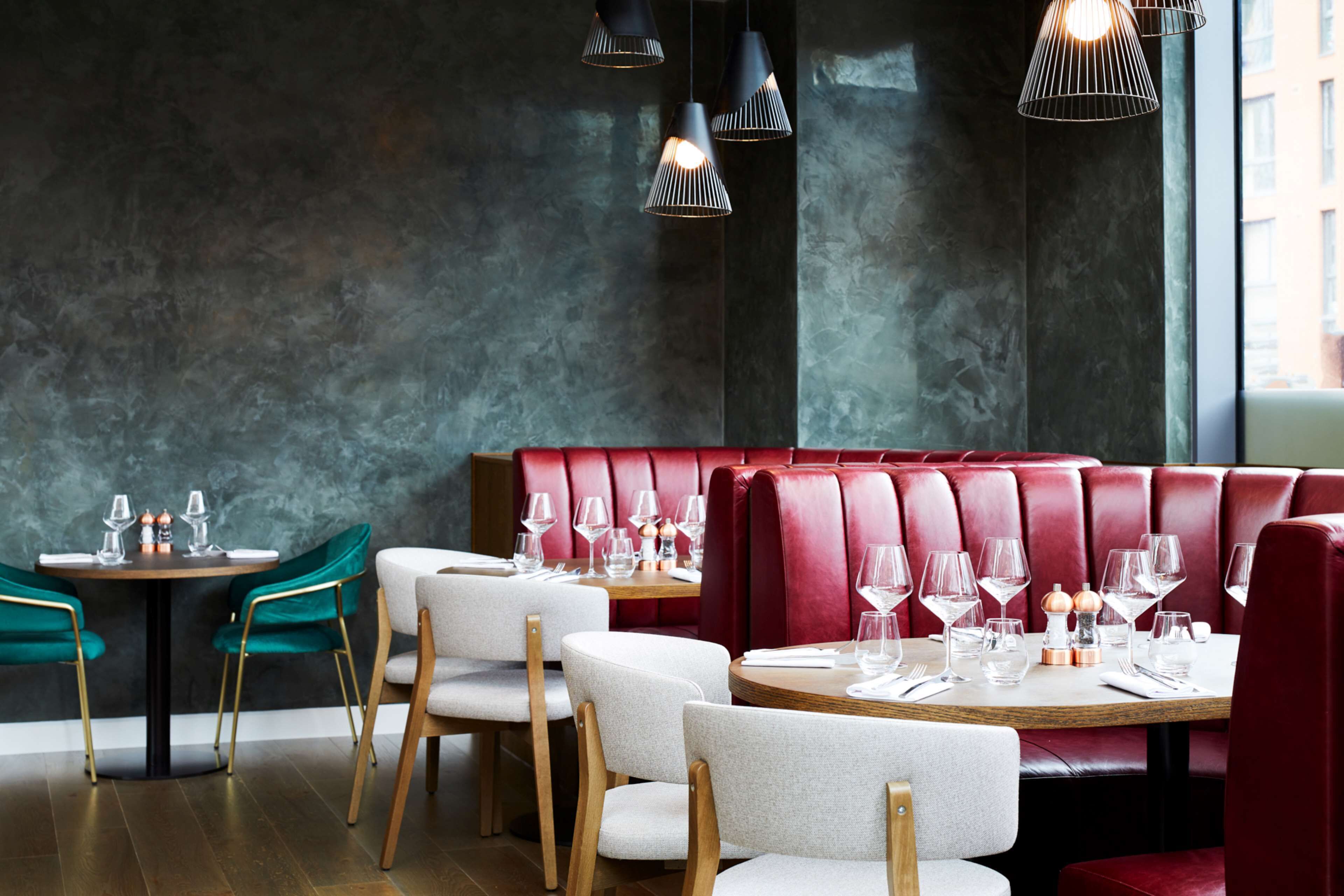 A restaurant interior with round tables, red upholstered booths, and green chairs.