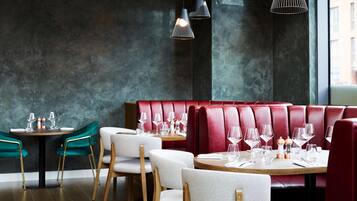 Un interior de restaurante con mesas redondas, asientos tapizados en rojo y sillas verdes.