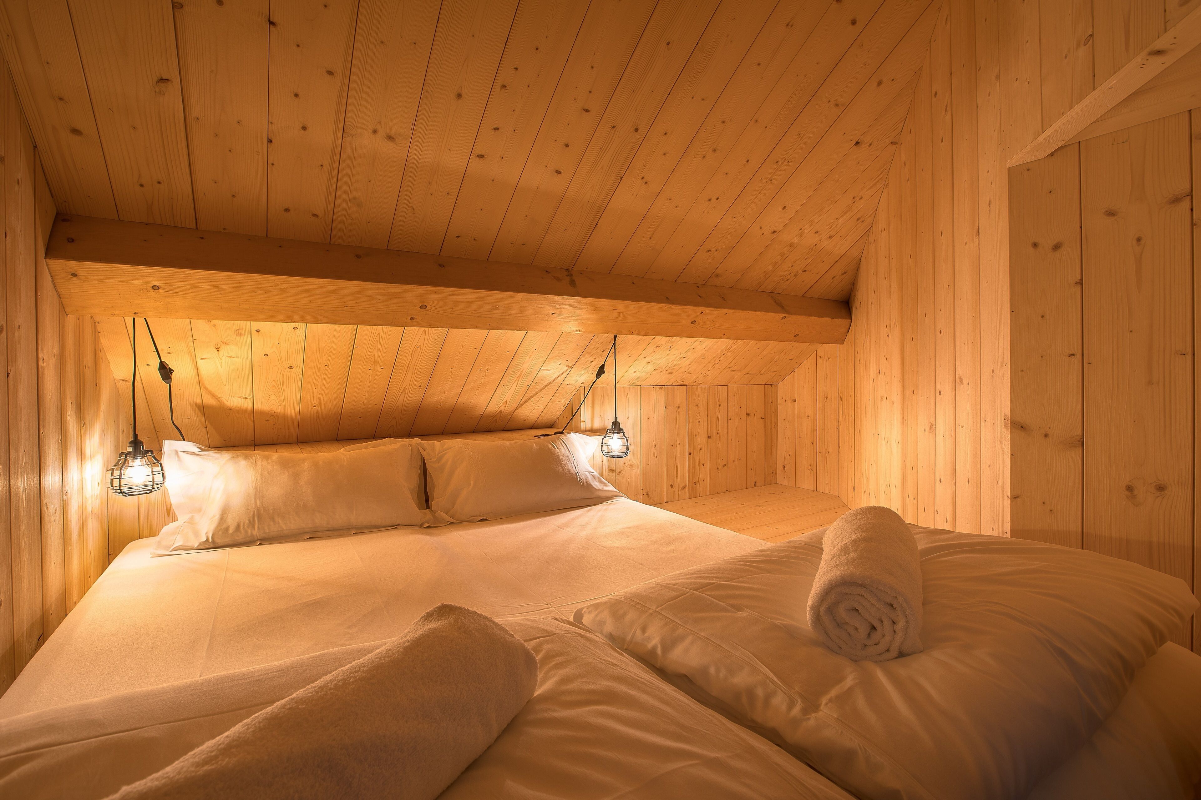 Une pièce chaleureuse, avec des murs en bois, un lit, deux lampes de chevet et une serviette pliée posée sur le lit.