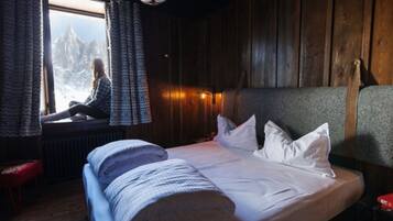 Une pièce confortable avec un lit, une fenêtre avec des rideaux et une vue sur les montagnes.